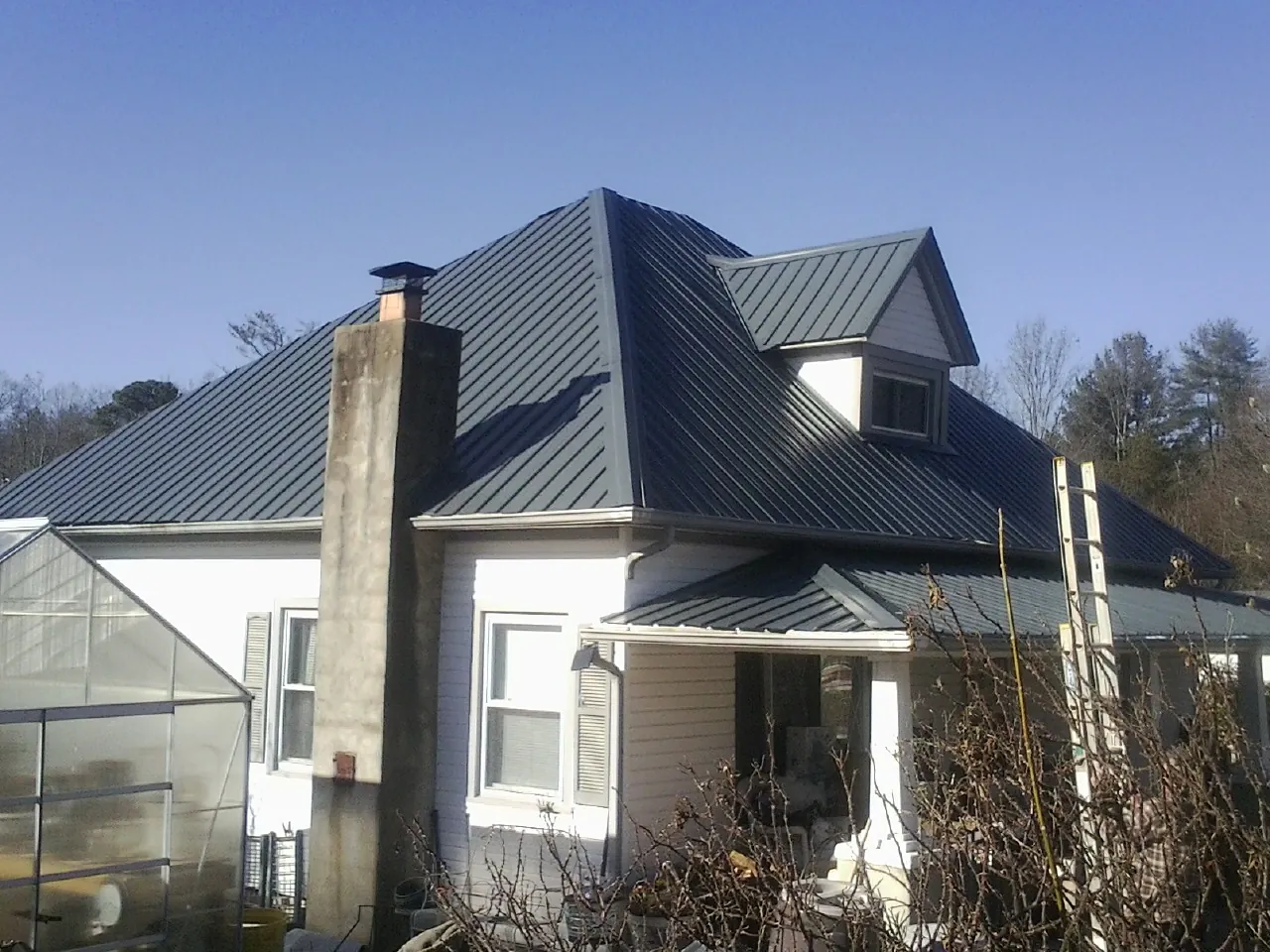 Dark blue standing seam metal roof on a white farmhouse with dormer — Slate & Tile Roof Repair by Roofing Brothers in Roma