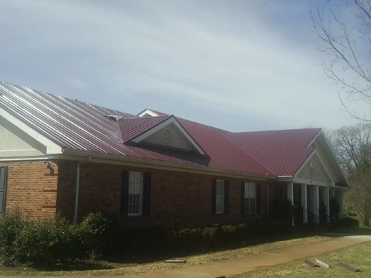 Red metal roof with gabled entries on a long brick building, from a Hail Damage Roof Repair job in Roma