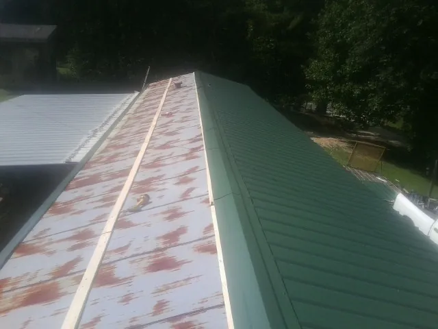 Old rusted panels beside newly installed green metal roofing — Wind Damage Roof Repair by Roofing Brothers in Roma