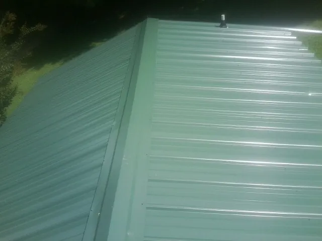 New green metal panels meeting at the ridge of a roof — Flat Roof Repair work by our crew in Roma
