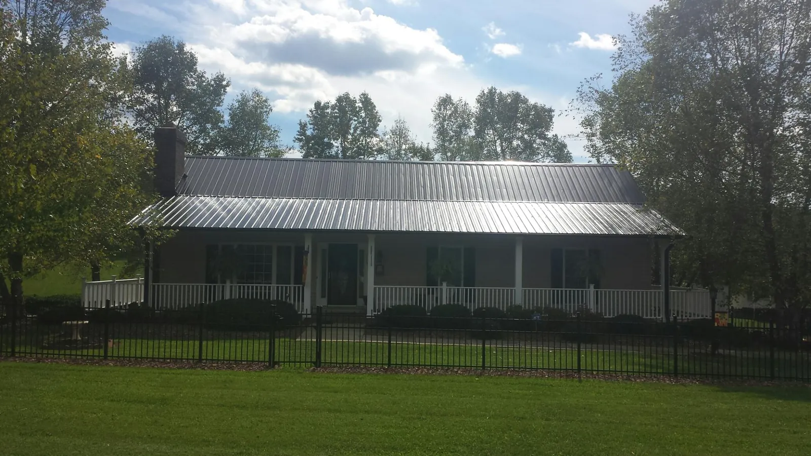 Gray metal roof on a brick ranch with a full width front porch — Gutter Guard Installation work by our crew in Roma